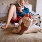 Injured man with bandaged foot using a tablet.