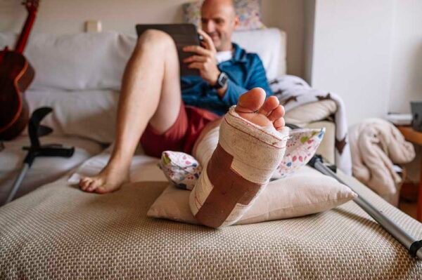 Injured man with bandaged foot using a tablet.