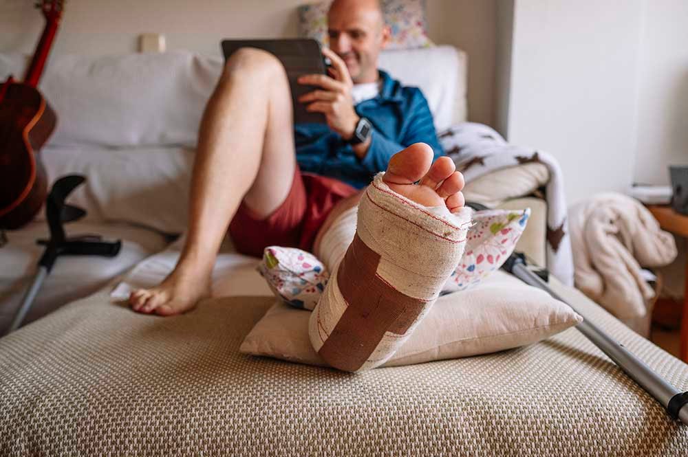 Injured man with bandaged foot using a tablet.