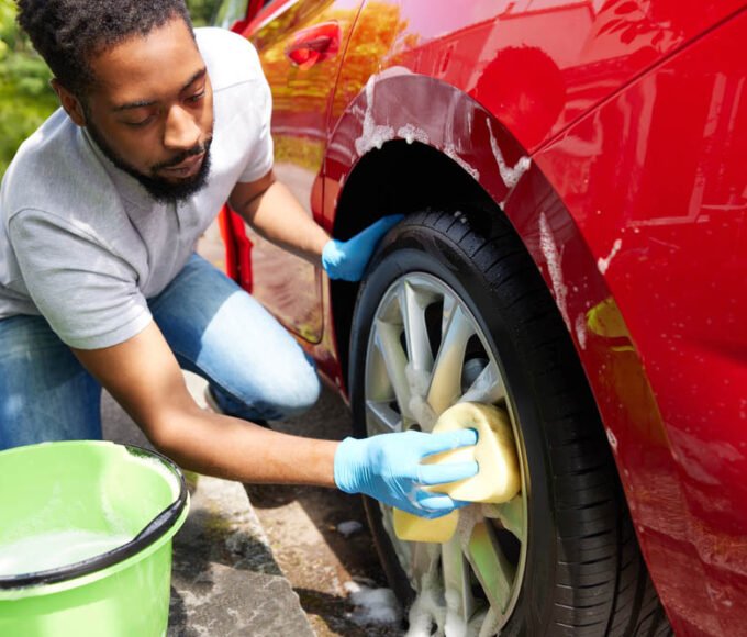 Man Washing Wheels Of Car During Valet Using Bucket And Sponge